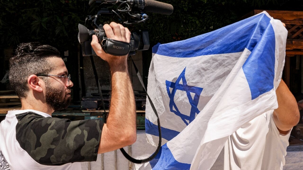 (FILES) An Israeli right-wing activist holds up an Israeli national flag to obscure the camera of a video journalist during the Jerusalem Day flag march