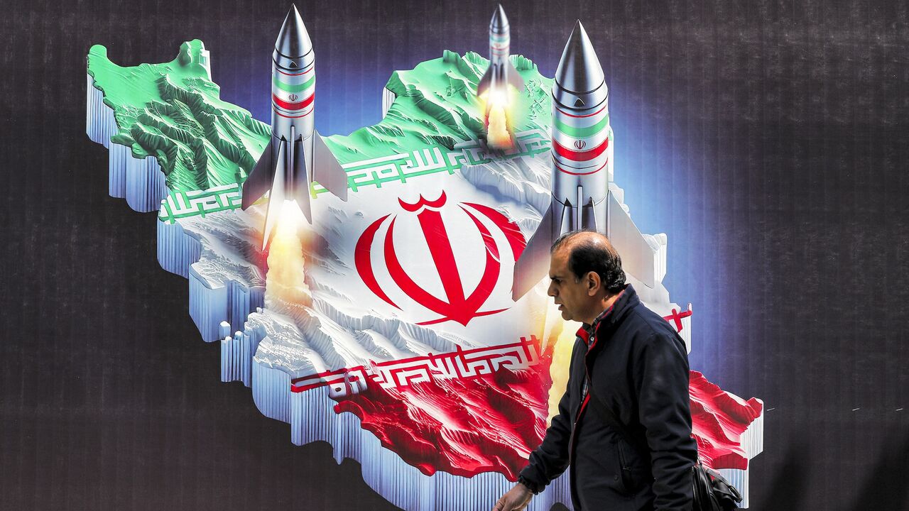 A man walks past a banner depicting missiles launching from a representation of the map of Iran colored with the Iranian flag in central Tehran on April 15, 2024.