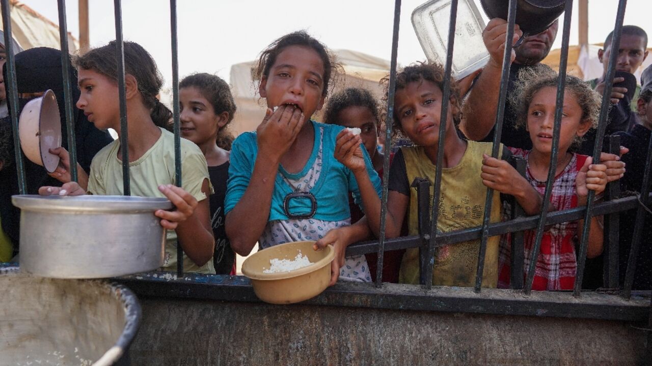 Palestinian children queue for cooked food rations at a makeshift Gaza displacement camp in Khan Yunis