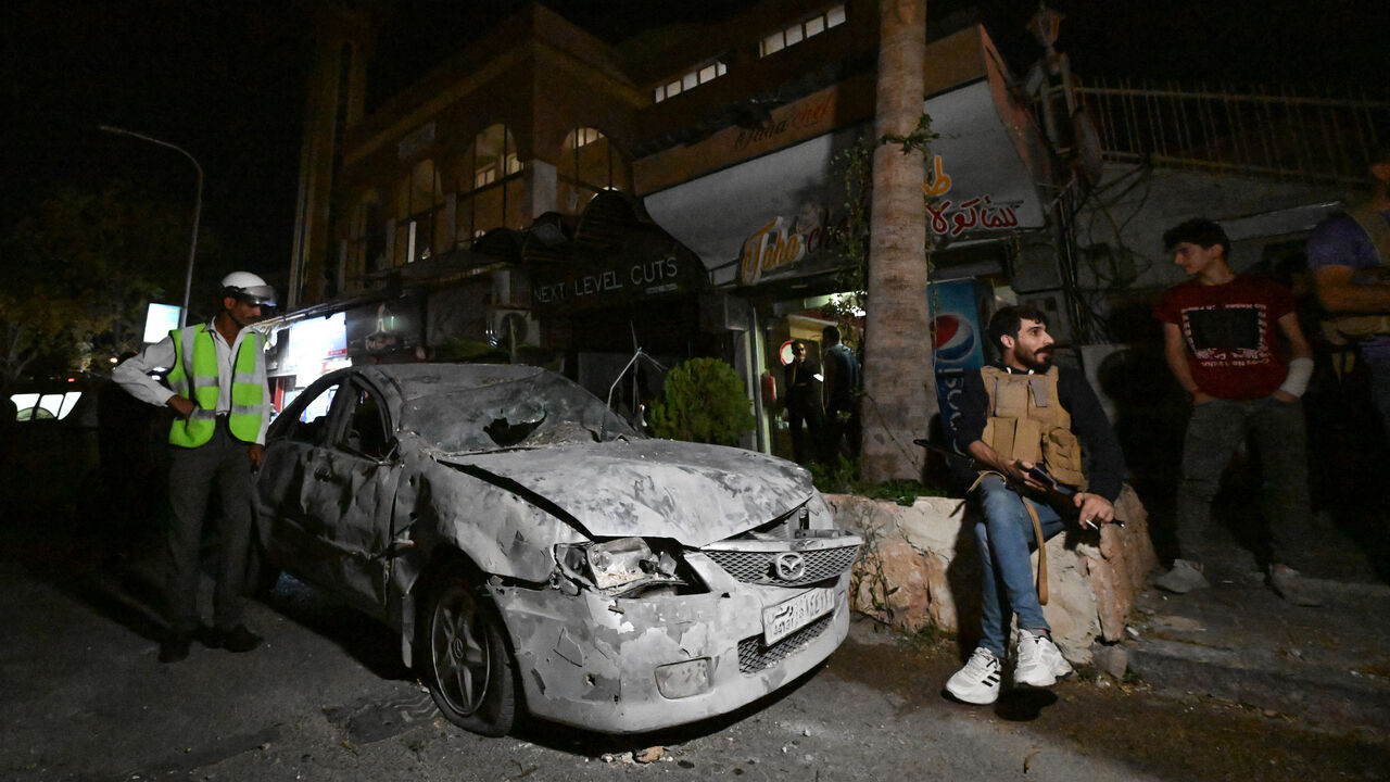 An armed man sits in front of a car damaged in a reported Israeli strike in Damascus on Oct. 2, 2024.