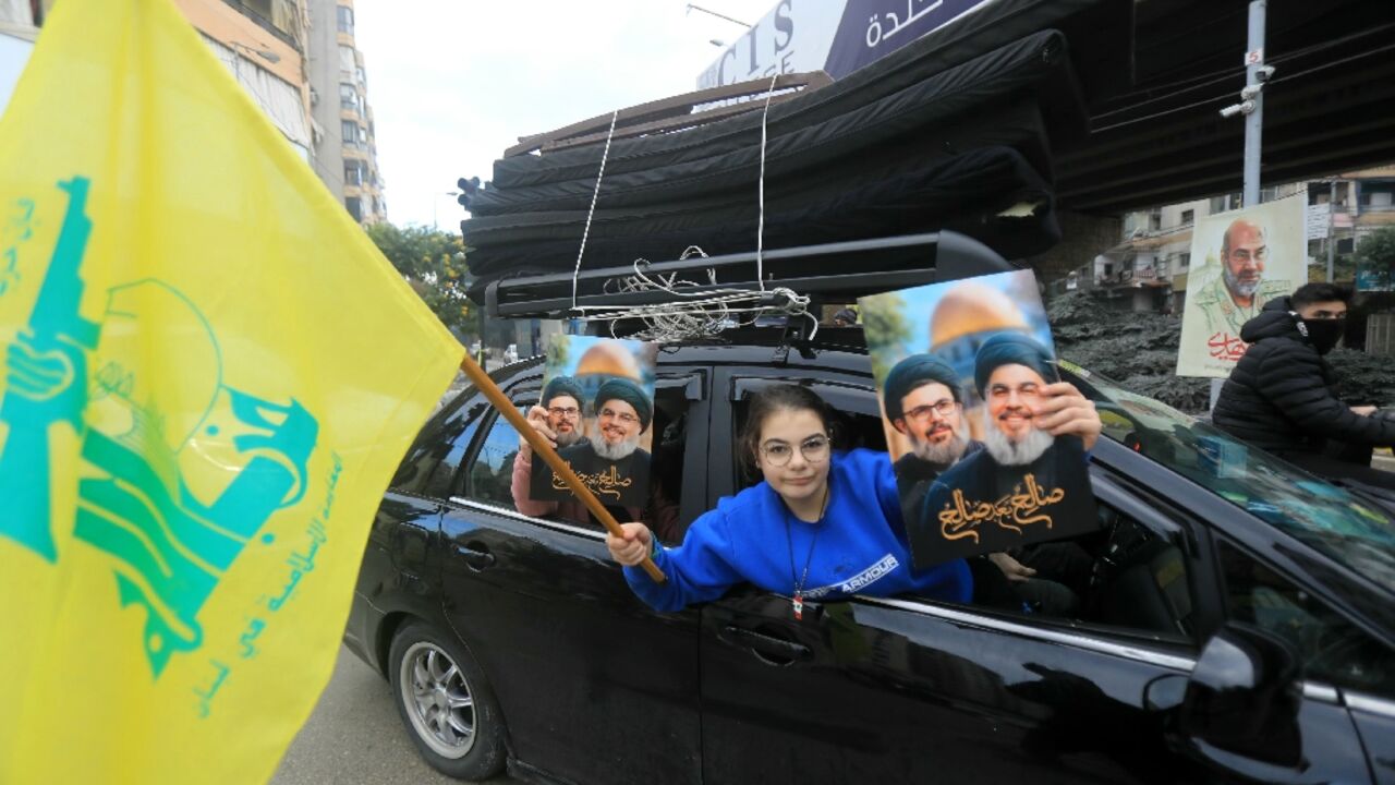 A Lebanese woman holds up portraits of Hezbollah's slain leaders Hassan Nasrallah and Hashem Safieddine along with the militant group's yellow flag as people return to Beirut's southern suburbs