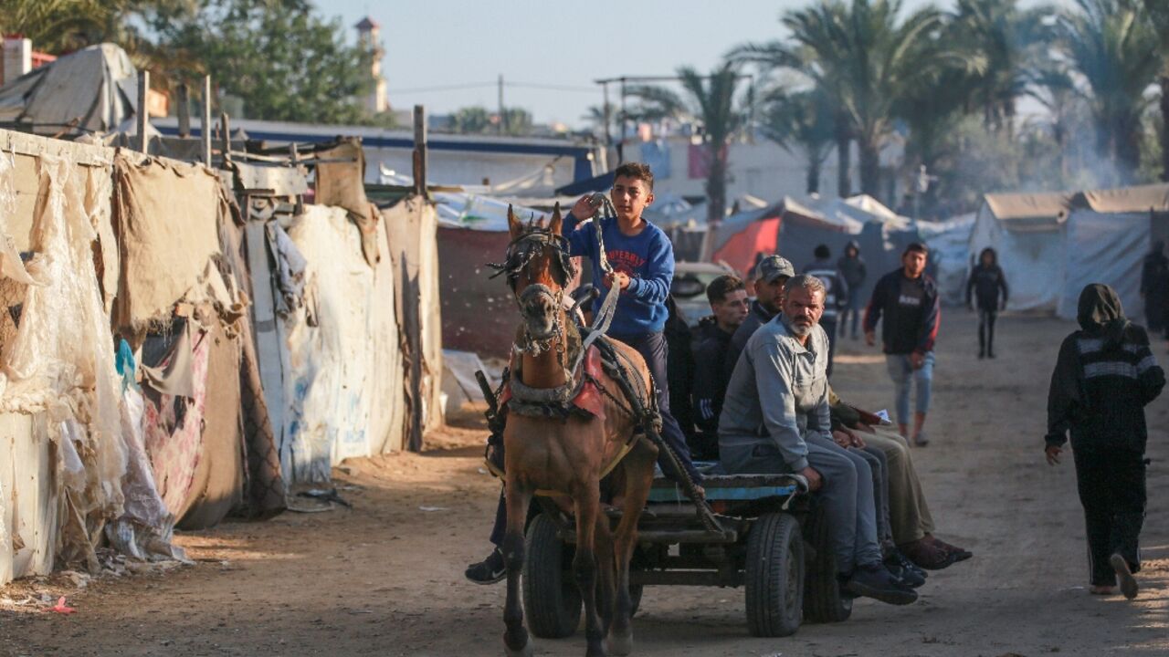 Displaced Palestinians using animal-drawn carts pass flimsy shelters in Al-Zawayda, central Gaza