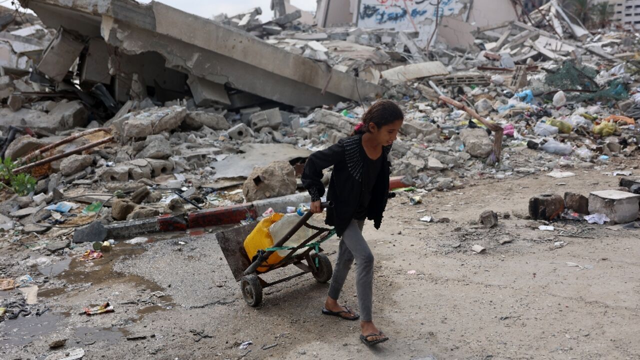 A Palestinian girl transports clean water past a destroyed building in Gaza City, in the territory's north