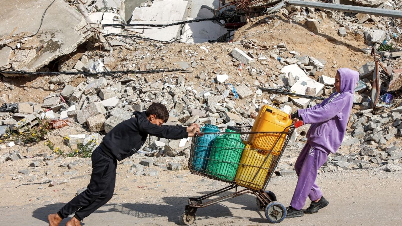 A girl pulls while a boy pushes a shopping-cart loaded with filled-up water containers past a mound of rubble and debris in Gaza City A girl pulls while a boy pushes a shopping-cart loaded with filled-up water containers past a mound of rubble and debris in Gaza City