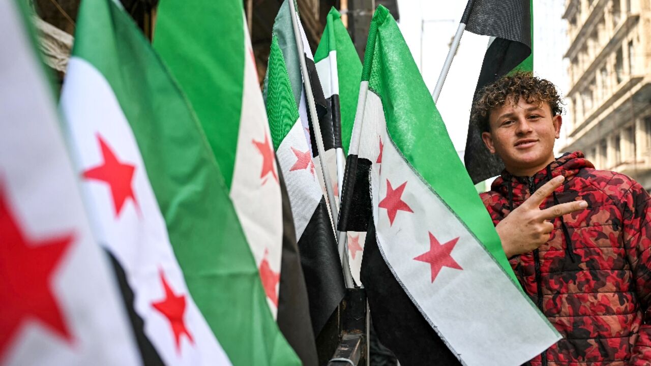 A man poses next to Syrian independence-era flags for sale at a stall in Aleppo city A man poses next to Syrian independence-era flags for sale at a stall in Aleppo city