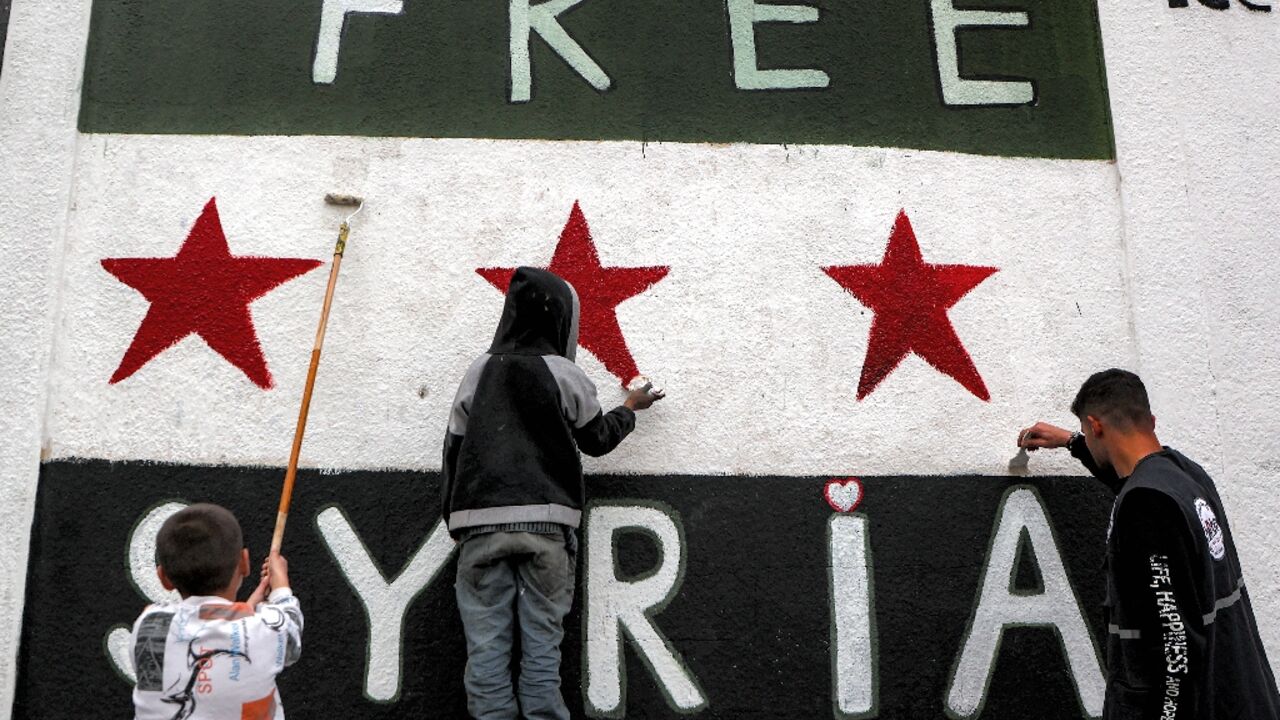 Syrians paint a mural of independence-era flag on a wall in the old city of Homs