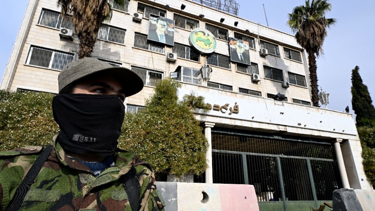 Portraits of toppled Syrian president Bashar al-Assad and his late father Hafez al-Assad hang outside Baath party offices in Damascus as a rebel fighter stands guard