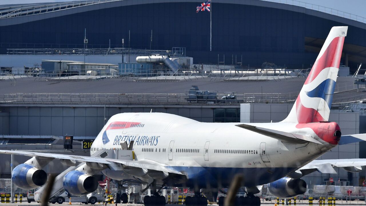 A Union flag flies above a hangar as a British Airways operated Airbus A747 passenger jet is moved by an aircraft tractor at Heathrow Airport, west of London on April 2, 2020, as life in Britain continues during the nationwide lockdown to combat the novel coronavirus COVID-19 pandemic.
