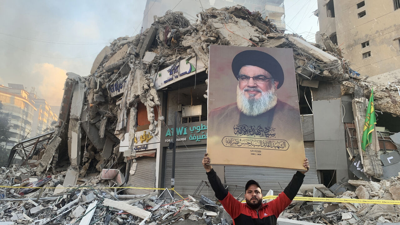 A man flashes a portrait of slain Hezbollah chief Hassan Nasrallah in front of the rubble of a building at the site of an Israeli airstrike in Beirut's southern suburbs, on November 12, 2024, amid the ongoing war between Israel and Hezbollah. (Photo by AFP) (Photo by -/AFP via Getty Images)