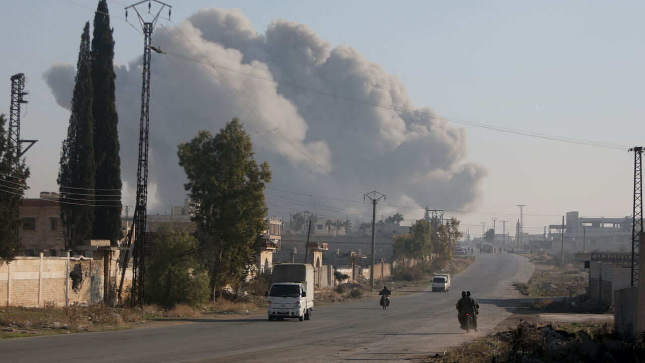 Fighters enter the Rashidin district on the outskirts of Aleppo on their motorbikes with smoke billowing in the background during fighting on Nov. 29, 2024, as Hayat Tahrir al-Sham (HTS) jihadists and allied factions continue their offensive in the Aleppo province against government forces.