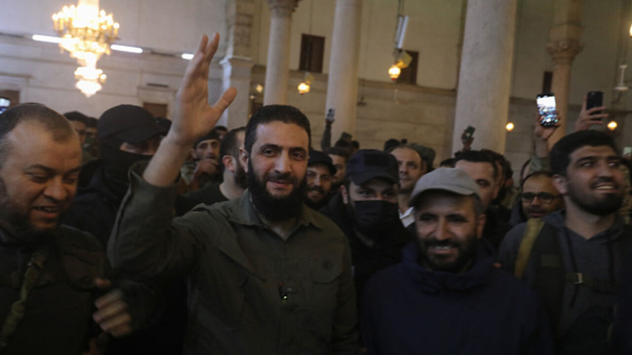 The leader of Syria's Islamist Hayat Tahrir al-Sham (HTS) group that headed a lightning rebel offensive snatching Damascus from government control, Abu Mohammed al-Jolani, waves to the crowd before addressing them at the capital's landmark Umayyad Mosque on December 8, 2024. Jolani, now using his real name Ahmed al-Sharaa, gave a speech as the crowd chanted "Allahu akbar (God is greatest)," a video shared by the rebels on their Telegram channel showed. (Photo by Abdulaziz KETAZ / AFP) (Photo by ABDULAZIZ KE