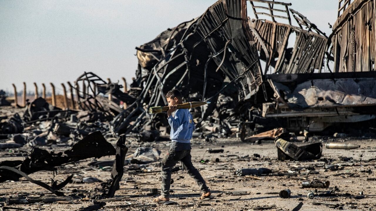 A boy carries an unexploded rocket propelled grenade at the site of an Israeli strike that weapons belonging to Syrian government forces