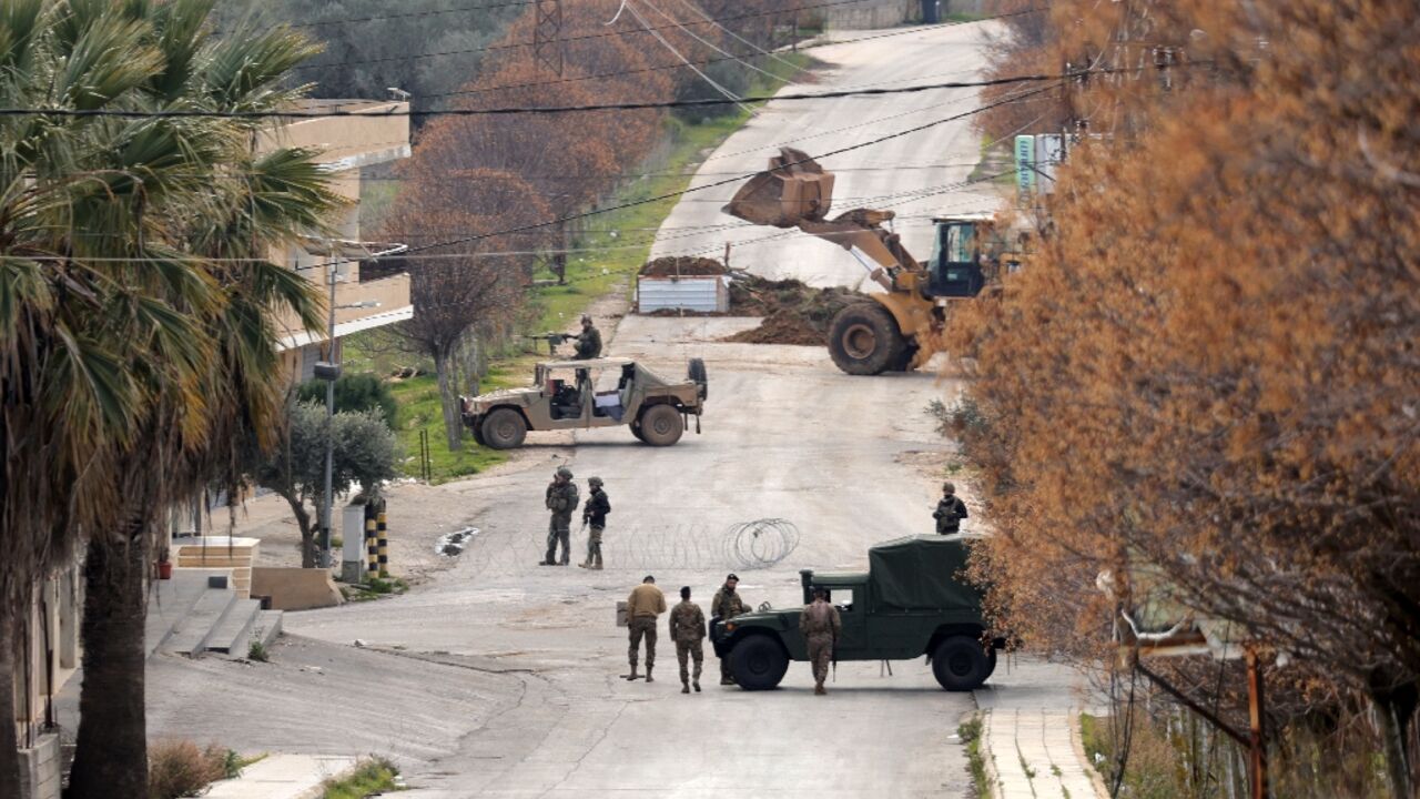 Lebanese army soldiers (R) and Israeli troops gather near their vehicles on either side of a barbed wire barrier, as an Israeli bulldozer pours soil to build a roadblock in Borj al-Mlouk in the border district of Marjayoun, southern Lebanon