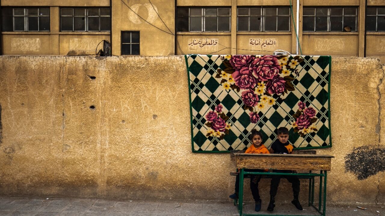 Children who fled ongoing battles between Turkish-backed groups and Syrian Kurdish forces in Syria's Aleppo province sit at a desk in the yard of a school in Hasakeh, where they and others took refuge