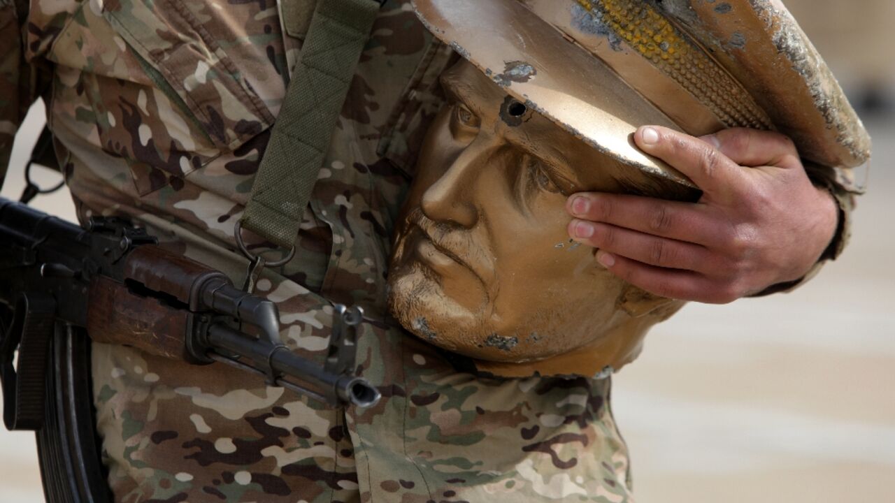 A fighter affiliated with Syria's new administration carries the decapitated head of an equestrian statue of Bassel al-Assad, brother of toppled president Bashar al-Assad, removed from the abandoned Republican Guard base on Mount Qasyun