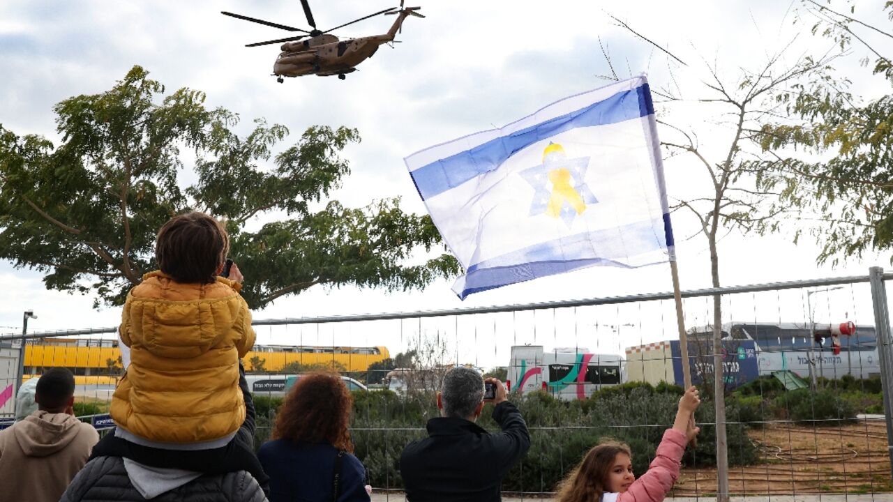 People wave an Israeli flag as they watch a military helicopter transporting a newly-released Israeli hostage, preparing to land at the Sheba hospital in Ramat Gan near Tel Aviv