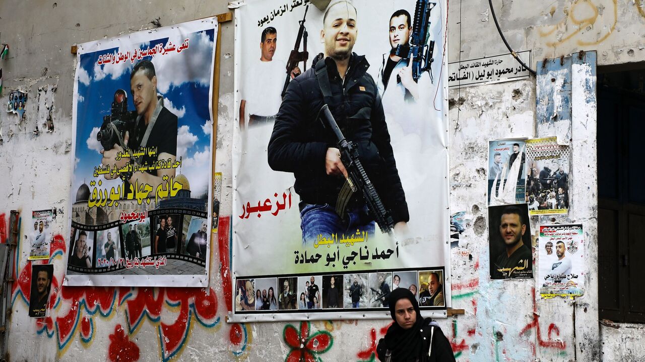A Palestinian woman stands against a wall plastered with posters picturing "martyrs" at a market in the Balata camp, near the occupied West Bank city of Nablus, on Dec. 15, 2020.