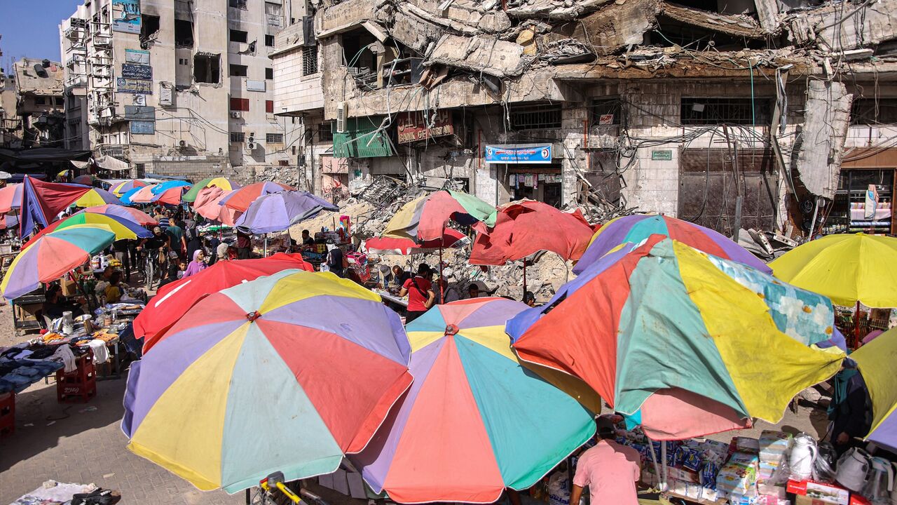 Vendors' umbrellas shade their stalls while erected before destroyed buildings along a market street in Gaza City, June 15, 2024.