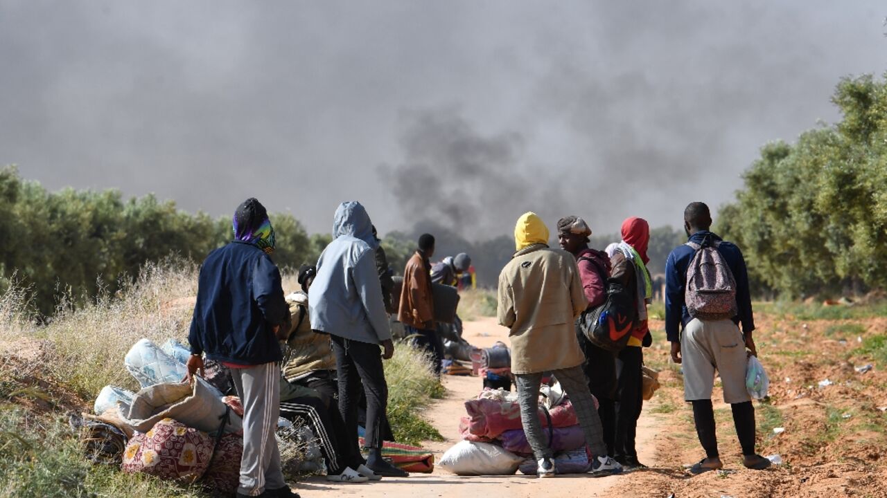 Migrants look on as smoke rises from what used to be their makeshift camp at El Amra Migrants look on as smoke rises from what used to be their makeshift camp at El Amra