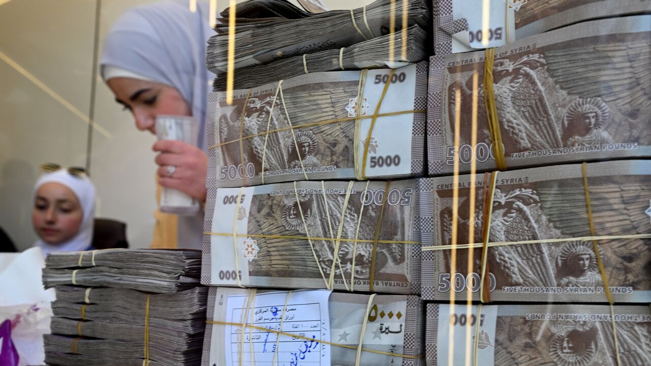 Employees stand behind stacks of local currency notes as they serve clients at an exchange shop in Damascus, on April 16, 2025.