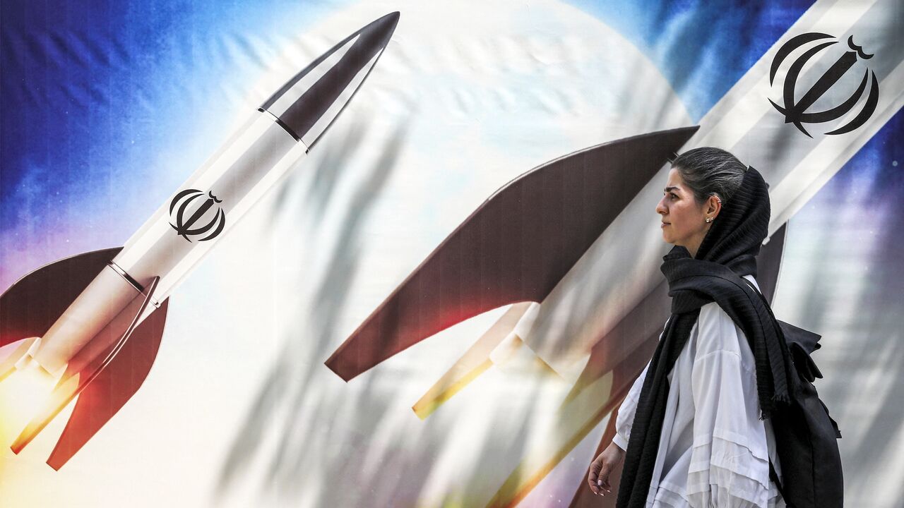 A woman walks past a banner depicting launching missiles bearing the emblem of the Islamic Republic of Iran in central Tehran on April 15, 2024.