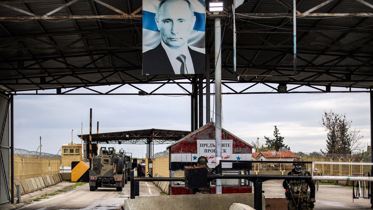 A portrait of Russia's President Vladimir Putin hangs above next to a torn out one of the ousted Syrian president, as Russian soldiers stand guard at the entrance of the Russian-leased Syrian military base of Hmeimim in Latakia province in western Syria on December 29, 2024.
