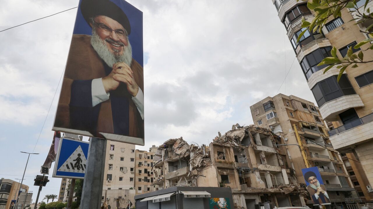 People drive on a street past portraits of slain Lebanese Hezbollah leader Hassan Nasrallah and buildings damaged in Israeli strikes in the recent war in the Ghobeiry neighborhood of Beirut's southern suburb on May 4, 2025.