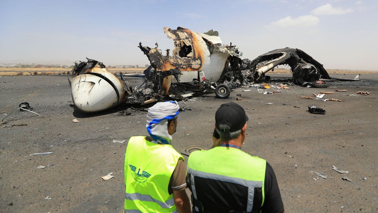 Airport employees stand next to a destroyed plane at the Sanaa International Airport on May 7, 2025, a day after Israel's military warplanes struck Yemen's rebel-held capital Sanaa.