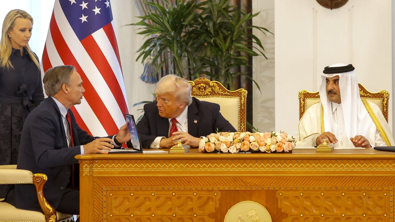Qatar's Emir Sheikh Tamim bin Hamad Al Thani (R) sits next to US President Donald Trump as he speaks to Boeing CEO Kelly Ortberg (L).