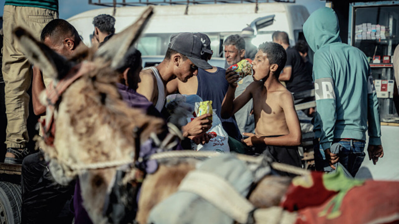 A hungry young boy eats raw noodles as dislocated Palestinians carry the humanitarian aid they have received from a United Nations distribution point in Rafah, southern Gaza Strip on May 27, 2025, following a chaotic incident in which Gazans stormed the aid center, leading to the withdrawal of the American company overseeing the operation after losing control of the situation. The scene underscores the desperation and urgency surrounding the humanitarian crisis as