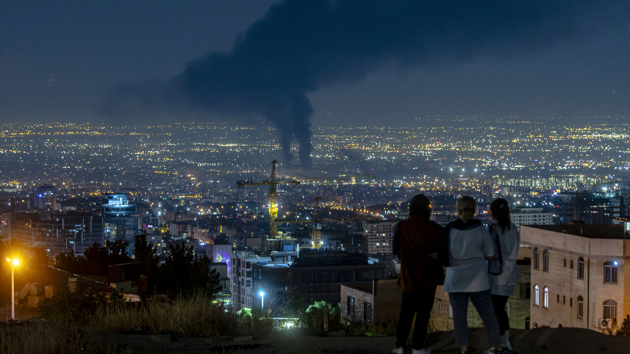 People gather on a hill to watch smoke rising in the distance from an Israeli airstrike in Tehran, Iran, on June 14, 2025.
