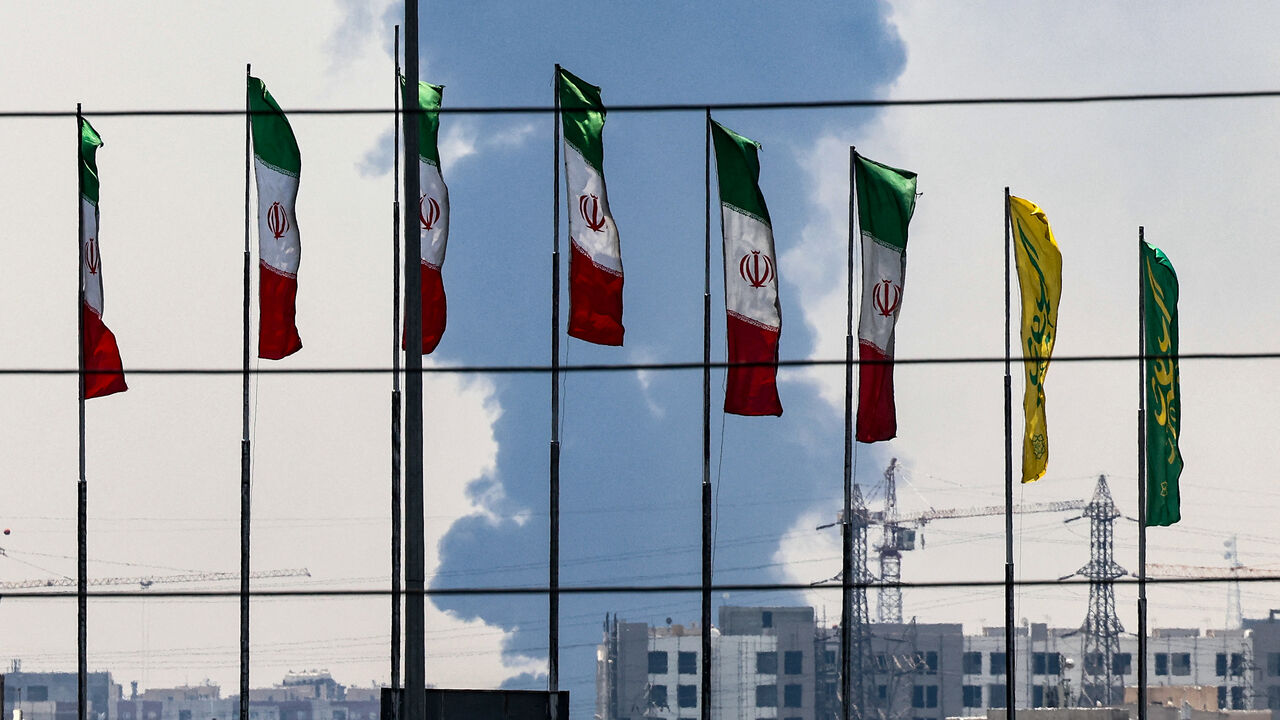 Flags flutter along a bridge as a plume of heavy smoke and fire rise from an oil refinery in southern Tehran, after it was hit in an overnight Israeli strike, on June 15, 2025. Iran fired a fresh barrage of missiles at Israel, state television announced early on June 15, as the rivals exchanged fire for a third day. (Photo by ATTA KENARE / AFP) (Photo by ATTA KENARE/AFP via Getty Images)