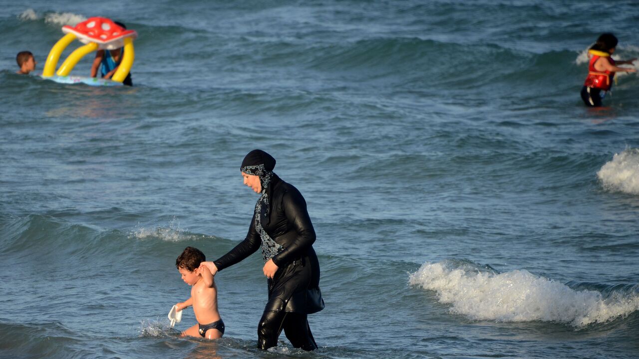 A Tunisian woman wearing a "burkini", a full-body swimsuit designed for Muslim women, walks in the water with a child on August 16, 2016 at Ghar El Melh beach near Bizerte, north-east of the capital Tunis. (Photo by FETHI BELAID / AFP) (Photo by FETHI BELAID/AFP via Getty Images)