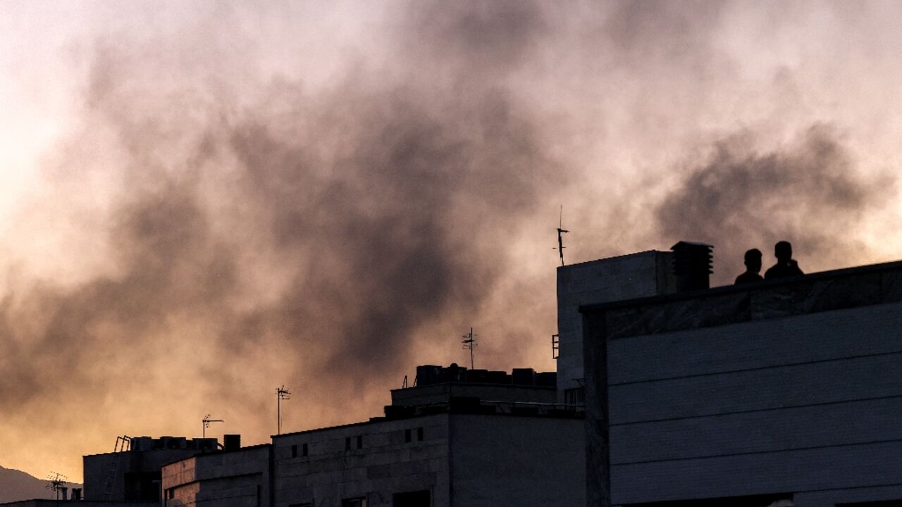 People stand on a rooftop as smoke wafts over Tehran following an Israeli strike People stand on a rooftop as smoke wafts over Tehran following an Israeli strike