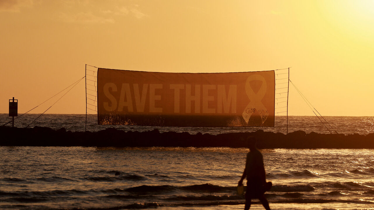 FILE PHOTO: A person walks on the beach, as a sign asks for the safe return of hostages held in Gaza since October 7, 2023 attack on Israel by Hamas, near the U.S. Consulate in Tel Aviv, Israel, July 7, 2025. REUTERS/Ammar Awad/File Photo