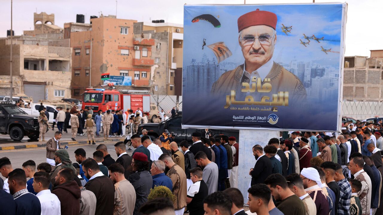 Security forces stand guard as Libyans perform the morning prayer of Eid al-Fitr with a portrait of the military strongman of eastern Libya, Khalifa Hiftar, in the background in the port city of Benghazi on March 31, 2025.