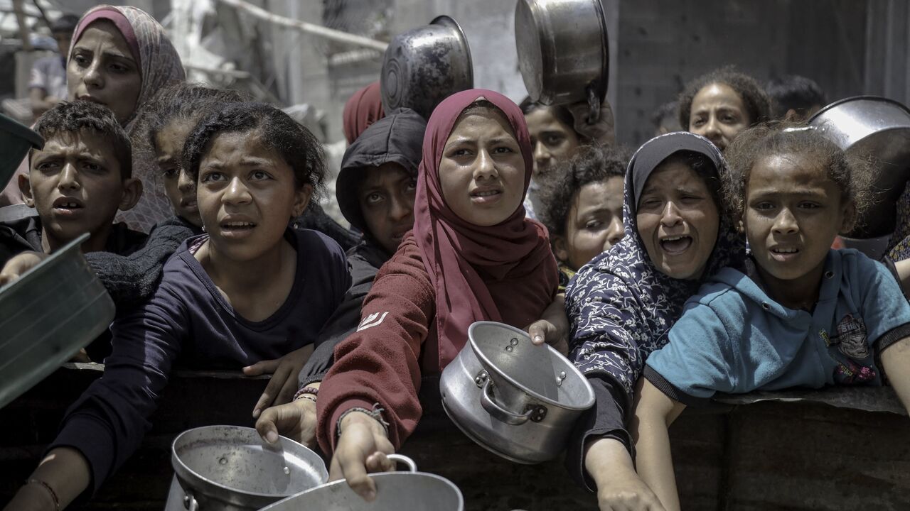 Women and children extend their arms with empty pots in Jabalia Refugee Camp, Gaza City, Gaza, on May 19, 2025.