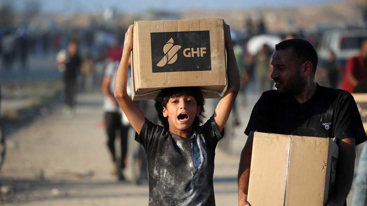 People carrying aid parcels walk along the Salah al-Din road near the Nusseirat refugee camp in the central Gaza Strip, used by food-seeking Palestinians to reach an aid distribution point set up by the privately run Gaza Humanitarian Foundation (GHF, on June 25, 2025.