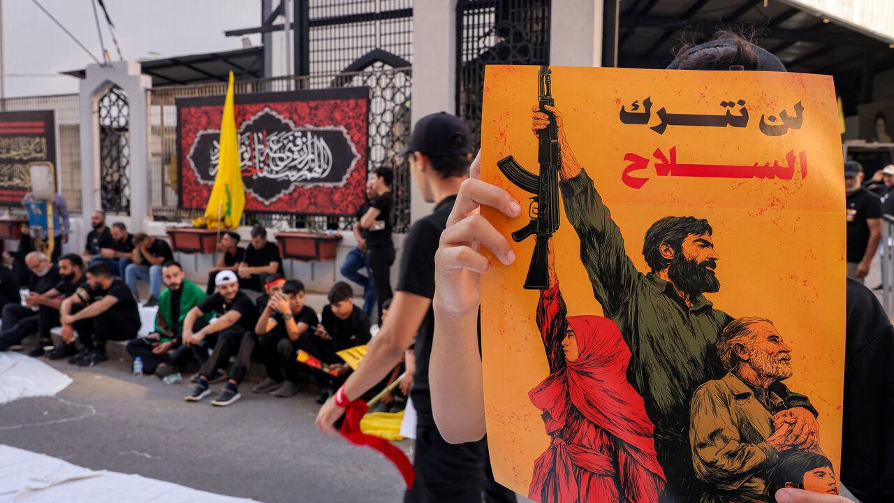 TOPSHOT - A person holds a sign with the Arabic slogan "we will not relinquish arms" as Lebanese Shiite Hezbollah supporters take part in a ceremony during the peak of Ashura, a 10-day period commemorating the seventh century killing of Prophet Mohammed's grandson Imam Hussein, in Beirut's southern suburbs on July 6, 2025. (Photo by ANWAR AMRO / AFP) (Photo by ANWAR AMRO/AFP via Getty Images)