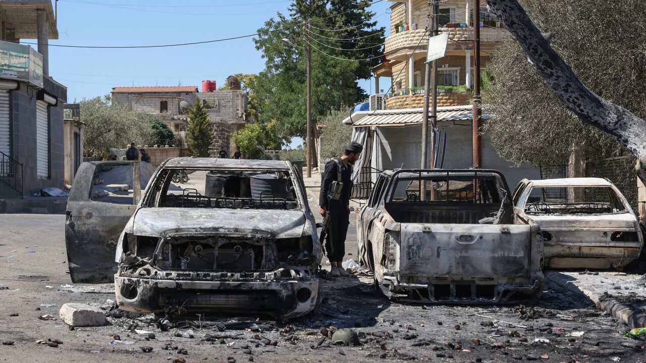 A member of the Syrian security forces examines burnt vehicles amid ongoing clashes in the southern Syrian city of Suwayda, July 16, 2025.