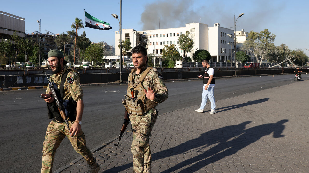 Syrian security forces stand guard in front of the heavily damaged Syrian army and defense ministry headquarters complex in Damascus, following Israeli strikes on July 16, 2025.