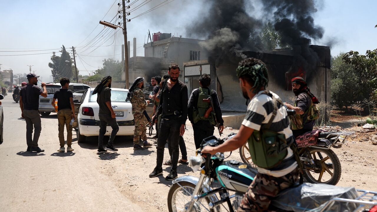 Fighters from Bedouin tribes gather near a burning building in al-Mazraa village, in Syria's southern Suwayda governorate, as clashes with Druze gunmen continue, on July 18, 2025. 