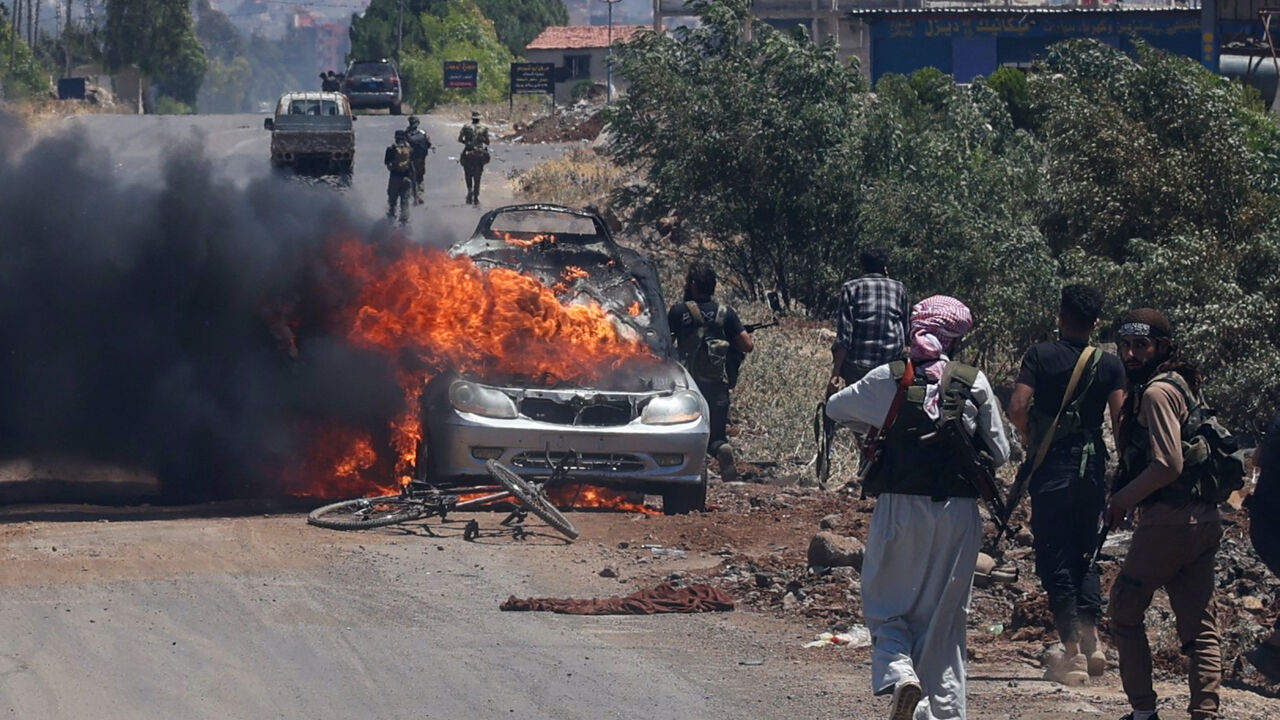 Bedouin and tribal fighters deploy as a car burns at the western entrance of Syria's Druze heartland of Suwayda on July 18, 2025.