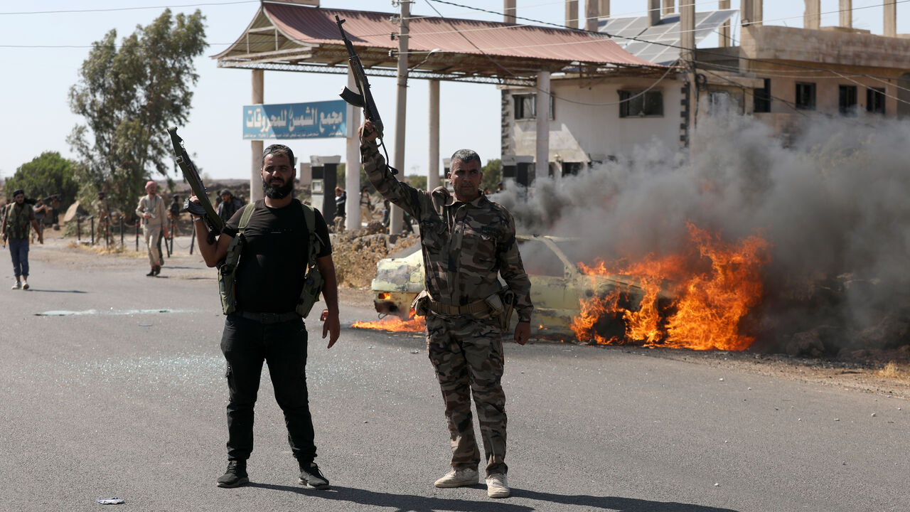 Two armed men gesture as a car burns near the site of clashes between Druze and Bedouin factions on July 14, 2025 in Suwayda, Syria.