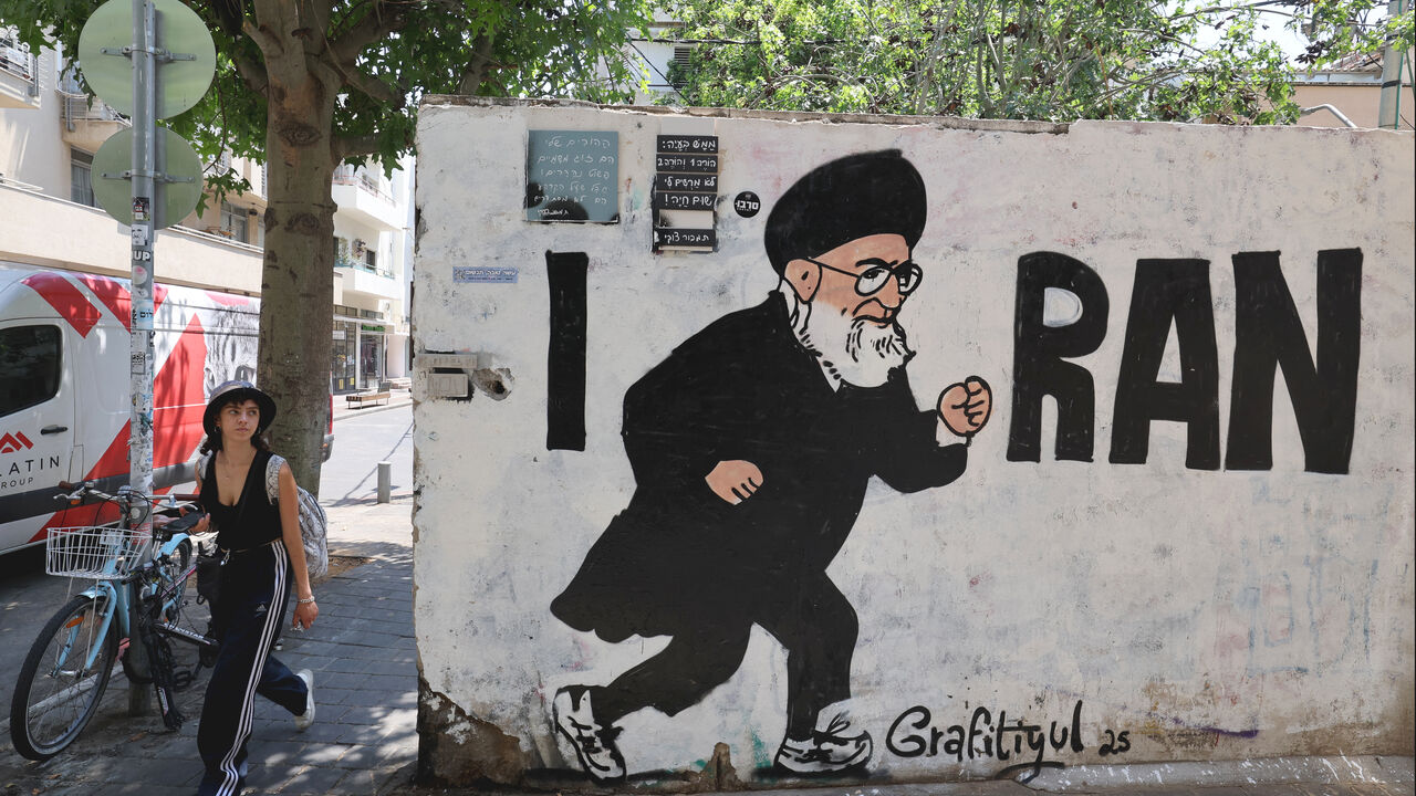 People walk past a mural drawn by the "Grafitiyul" graffiti art group depicting Iran's Supreme Leader Ayatollah Ali Khamenei, on a street in the Israeli coastal city of Tel Aviv on July 22, 2025. (Photo by JACK GUEZ / AFP) / RESTRICTED TO EDITORIAL USE - MANDATORY MENTION OF THE ARTIST UPON PUBLICATION - TO ILLUSTRATE THE EVENT AS SPECIFIED IN THE CAPTION (Photo by JACK GUEZ/AFP via Getty Images)