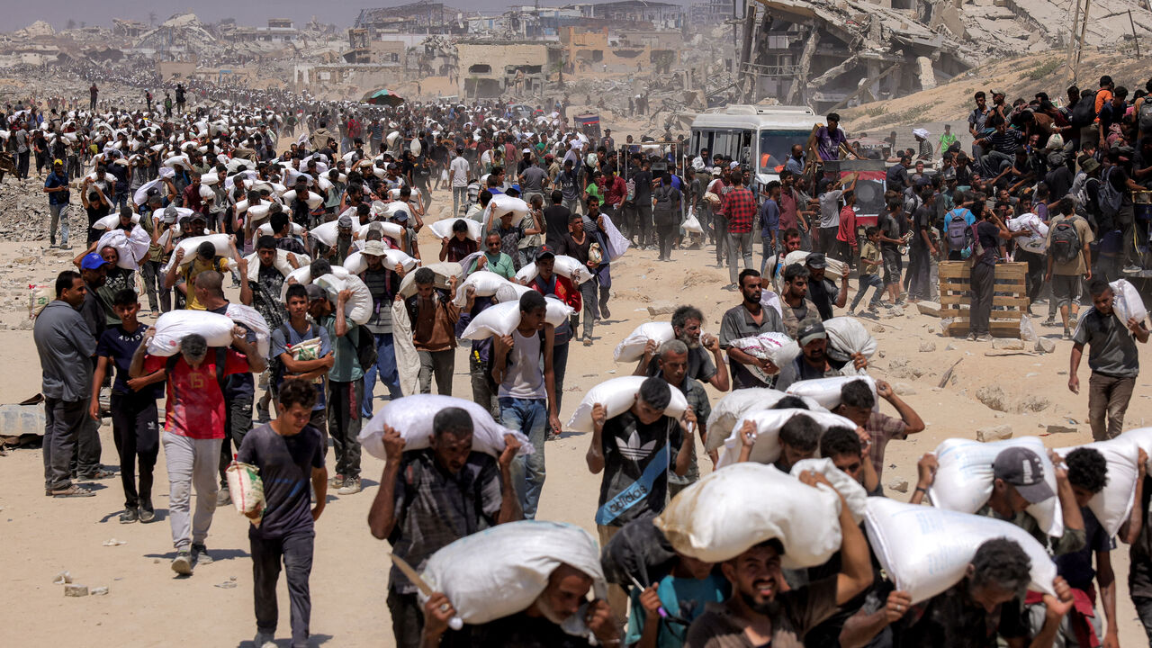 TOPSHOT - People walk with sacks of flour delivered after trucks carrying humanitarian aid entered northern Gaza on July 27, 2025 coming from the Zikim border crossing. (Photo by BASHAR TALEB / AFP) (Photo by BASHAR TALEB/AFP via Getty Images)