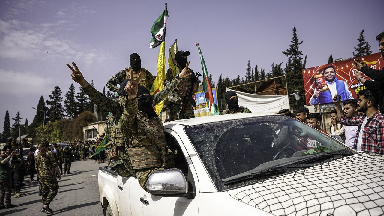 SDF fighters wave flags and flash victory signs from a vehicle during a convoy procession in Aleppo, Syria, on April 9, 2025.