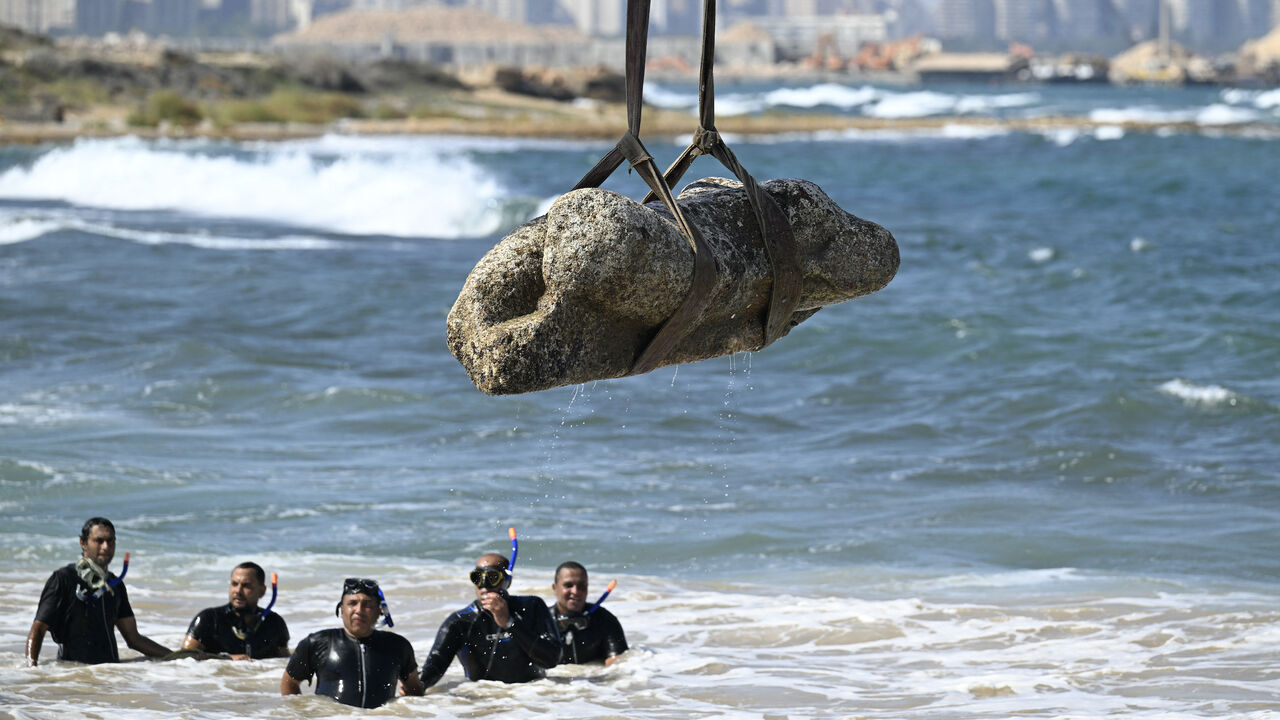 Divers watch as a crane pulls an artifact from the waters at Abu Qir bay in Alexandria on Aug. 21, 2025, as part of an event organized by the Ministry of Tourism and Antiquities to recover sunken antiquities.