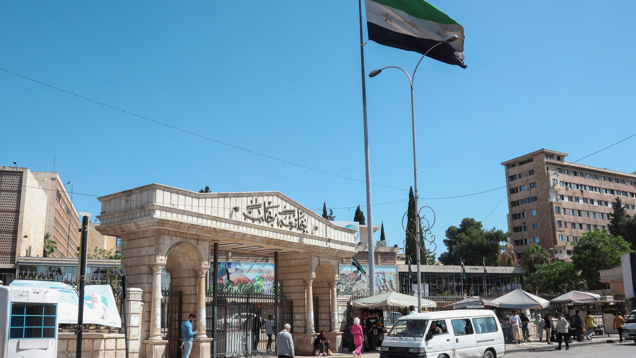 FILE PHOTO: People walk near the Syrian flag in Aleppo, Syria May 14, 2025. REUTERS/Mahmoud Hassano