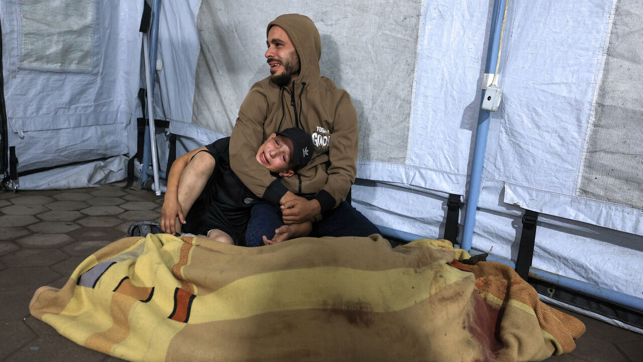 A man and a child mourn by the covered body of a Palestinian killed in an Israeli air strike, according to medics, at Al-Ahli Arab Hospital in Gaza City November 19, 2025. REUTERS/Dawoud Abu Alkas